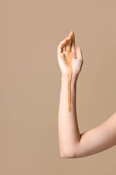 vrouw met druipende honing op haar hand tegen beige achtergrond - Foto, afbeelding