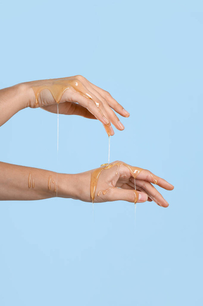 Woman with dripping honey on her hands against blue background - Foto, immagini