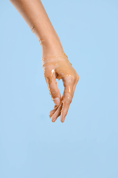 Woman with dripping honey on her hand against blue background - Фото, изображение