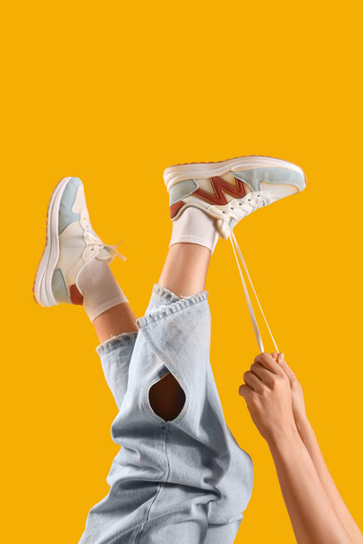 Женщина в стильных кроссовках, завязывающая шнурки на цветном фоне, крупным планом - Фото, изображение