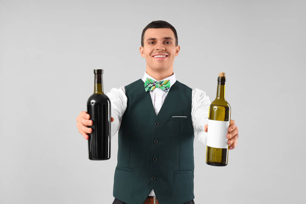 Jovem barman com garrafas de vinho em fundo cinza - Foto, Imagem