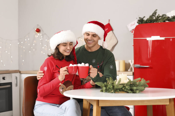 Jong stel drinken warme chocolademelk met marshmallows in de keuken op kerstavond - Foto, afbeelding