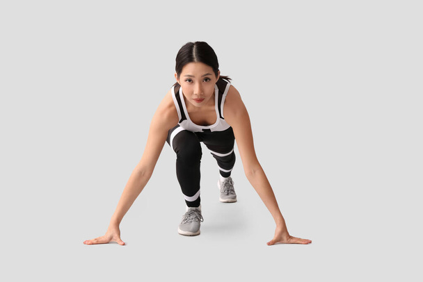 Sporty young Asian woman getting ready to run on light background - Photo, Image