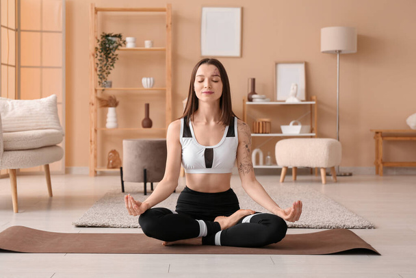 Sportos fiatal nő meditál szőnyegen otthon - Fotó, kép