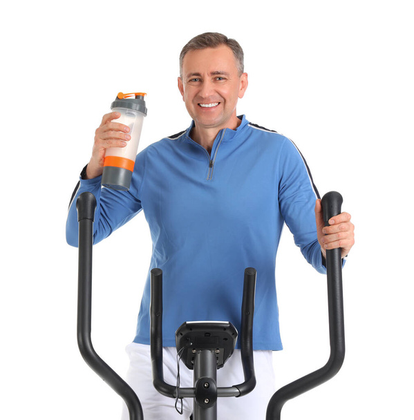 Sportlicher reifer Mann mit Wasserflasche auf dem Heimtrainer vor weißem Hintergrund - Foto, Bild