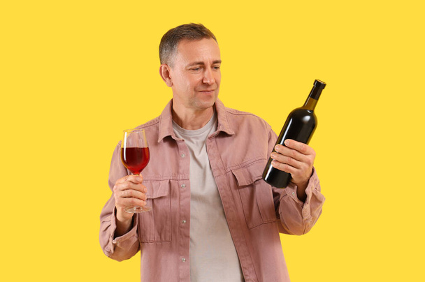 Uomo maturo con bicchiere e bottiglia di vino rosso su sfondo giallo - Foto, immagini