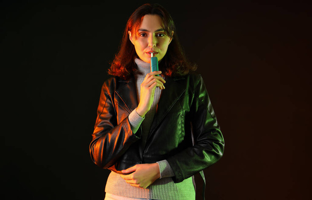 Mujer joven fumando cigarro electrónico sobre fondo oscuro - Foto, Imagen