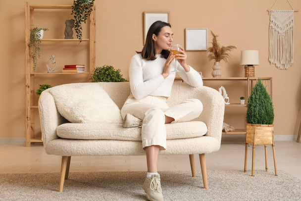 Όμορφη γυναίκα με ένα ποτήρι κρασί κάθεται στον καναπέ στο σπίτι - Φωτογραφία, εικόνα