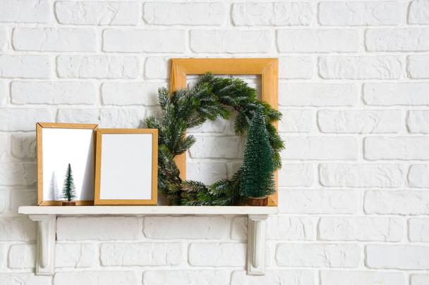 白い煉瓦の壁に掛かっている空白の写真のフレームおよびクリスマスの羽が付いている棚 - 写真・画像