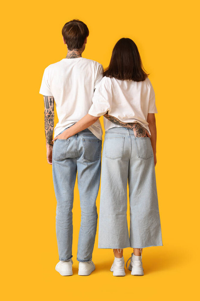 Pareja joven en jeans con estilo sobre fondo amarillo, vista trasera - Foto, Imagen