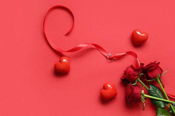 Όμορφη σύνθεση με δαχτυλίδι αρραβώνων και τριαντάφυλλο λουλούδια σε κόκκινο φόντο. Γιορτή του Αγίου Βαλεντίνου - Φωτογραφία, εικόνα