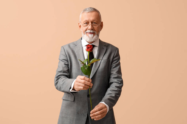 Зрілий чоловік з трояндовою квіткою на день Святого Валентина на бежевому фоні - Фото, зображення