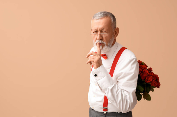 Volwassen man met boeket rozen met stille gebaar op beige achtergrond. Valentijnsdag - Foto, afbeelding