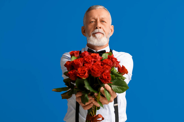 Hombre maduro con ramo de rosas sobre fondo azul. Celebración de San Valentín - Foto, Imagen