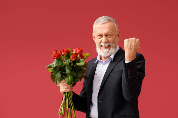 Vrolijke volwassen man met boeket rozen op rode achtergrond. Valentijnsdag - Foto, afbeelding