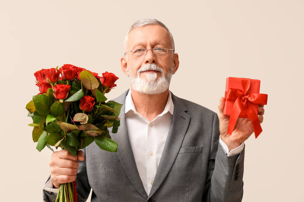 Happy mature man with bouquet of roses and gift for Valentine's day on white background - Photo, Image