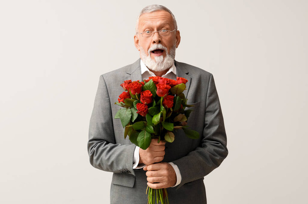 Geschokt volwassen man met boeket rozen op witte achtergrond. Valentijnsdag - Foto, afbeelding