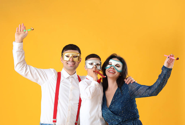 Счастливая семья в карнавальных масках с праздничными свистками на желтом фоне - Фото, изображение