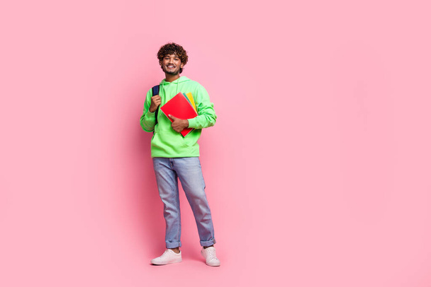 Full body photo of young indian student guy in green trendy sweatshirt with rucksack behind hold books isolated on pink color background. - Zdjęcie, obraz