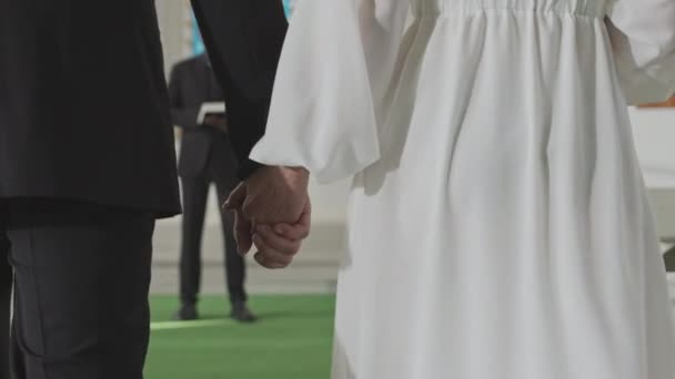 Mittelteil Rückseite Slowmo von unkenntlich Braut und Bräutigam Händchen haltend, während sie sich dem afroamerikanischen männlichen Beamten nähern, der gemütliche Trauung in der Kapelle - Filmmaterial, Video