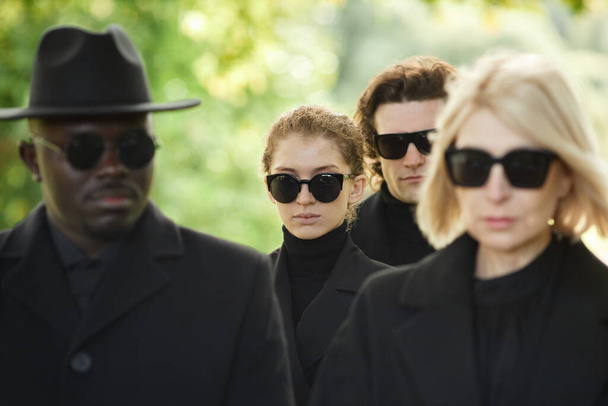屋外の葬儀で沈黙のうちに立っているサングラスで黒を着用する人々のグループ - 写真・画像