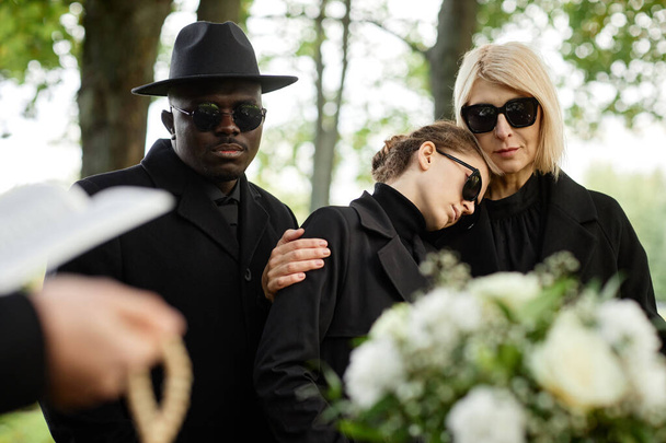 Porträt von Mutter und Tochter, die sich bei einer Beerdigungszeremonie im Freien umarmen und gemeinsam trauern - Foto, Bild