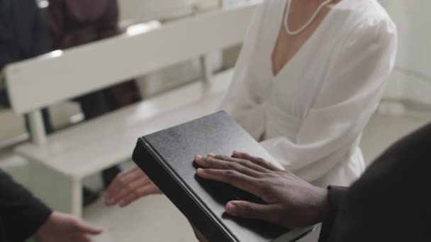 Gekippte Aufnahme eines kaukasischen Paares mittleren Alters, das Eheringe austauscht, während es neben seinem schwarzen männlichen Beamten steht, der Hand an Bibelbuch hält und erwachsenen Kindern zusieht, wie sie von einer Bank aus zusehen - Filmmaterial, Video