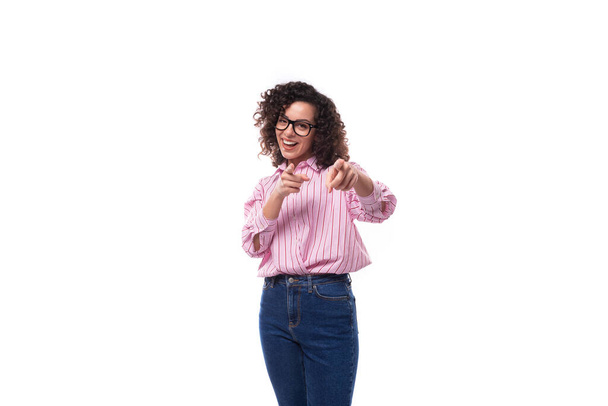 young pretty lady with curly black hair in a pink blouse and jeans on a white background with copy space. - Photo, Image