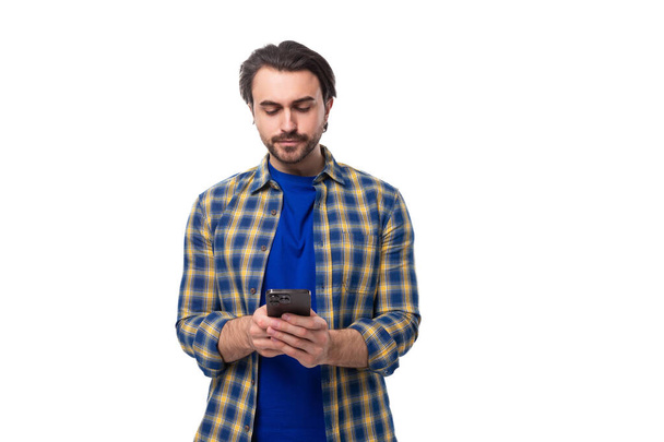 elegante bem tratado morena brutal homem com uma barba em uma camisa xadrez lê uma mensagem em um smartphone. - Foto, Imagem