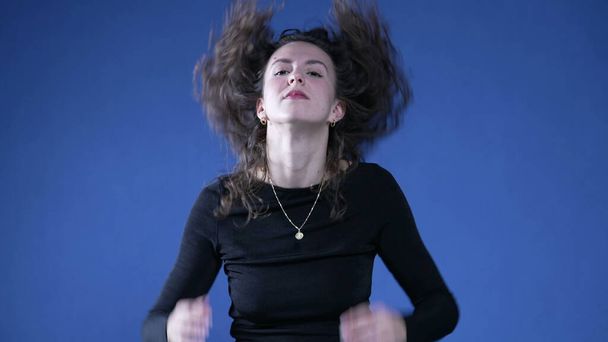 Mujer jugando con su pelo temblando mientras está de pie sobre fondo azul - Foto, Imagen