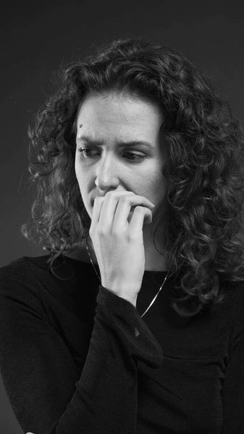 Verzweifelte Frau, die mit lähmender Angst kämpft, indem sie Nägel beißt und vergangene Ereignisse in dramatischen monochromen Schwarz-Weiß wiederkäut  - Foto, Bild