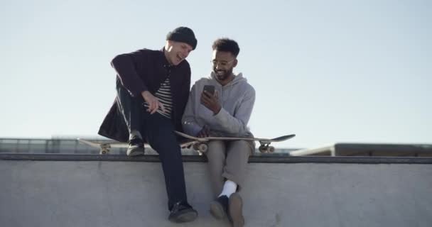 Κινητό τηλέφωνο, skateboard και τους άνδρες φίλους στην πόλη κάθεται σε μια ταράτσα κτιρίου κύλιση στα μέσα κοινωνικής δικτύωσης. Αστεία, υπαίθρια και νέους άνδρες γέλιο κατά την περιήγηση στο κινητό app με τηλέφωνο στο πάρκο skate - Πλάνα, βίντεο