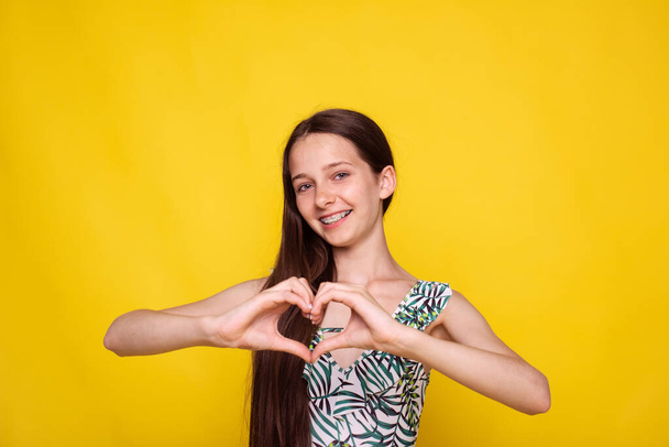 Teenie-Mädchen mit Zahnspange zeigen Geste Herzform von Händen auf gelbem Hintergrund - Foto, Bild