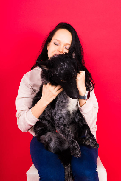 Szczęśliwa pani w casual nosić przytulanie czystorasowy pies, błotnisty z właścicielem na tle studio. - Zdjęcie, obraz