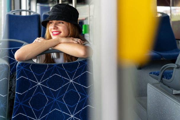 Şık genç bir kadın otobüsün içinde gülümsüyor, kentsel yaşam tarzını kucaklıyor. Şehre gidiş-dönüş Neşe. - Fotoğraf, Görsel