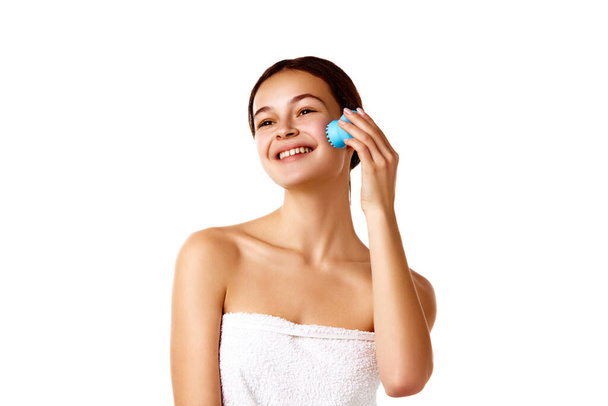 Shower routine. Smiling tender young girl cleansing face with washing brush against white background. Concept of natural female beauty, skin care, cosmetology and cosmetics - Photo, Image