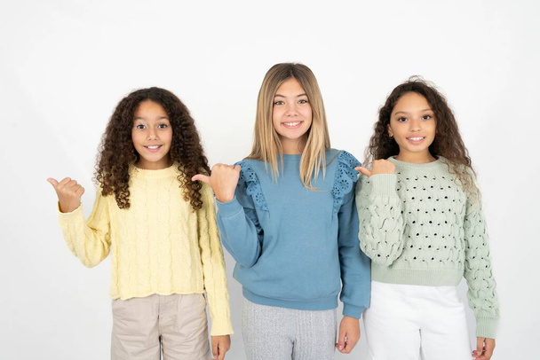 Mooie drie tiener meisjes wijzen opzij met wijsvinger, tonen op kopieerruimte met nieuws over koopjes - Foto, afbeelding