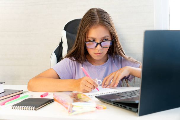 Δημοτικό σχολείο Παιδί μαθητής γράφει στο βιβλίο χρησιμοποιώντας φορητό υπολογιστή. Εκπαίδευση εξ αποστάσεως σε απευθείας σύνδεση. Μαθητής κορίτσι σπουδάζει στο σπίτι με ψηφιακή ταμπλέτα υπολογιστή και να κάνει σχολική εργασία. - Φωτογραφία, εικόνα