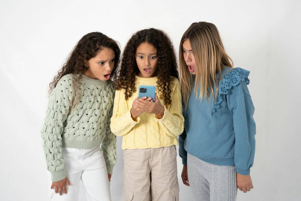 Yllättynyt kolme teini-ikäistä tyttöä, jotka käyttävät älypuhelinta lukemalla sosiaalisen median uutisia tai tärkeää sähköpostia - Valokuva, kuva
