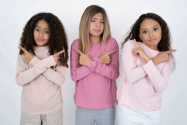 three teenager girls crosses arms and points at different sides hesitates between two items or variants. Needs help with decision - Photo, Image