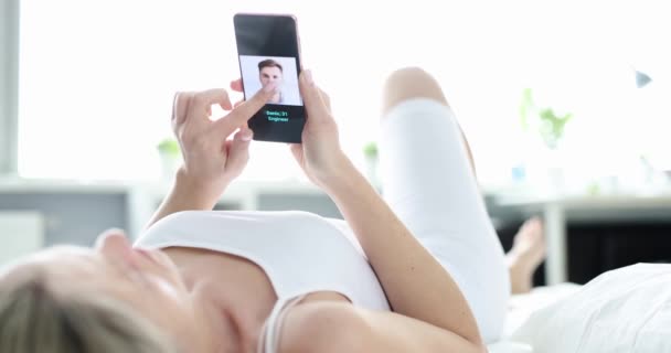 Een vrouw op bed kiest een man in een online applicatie op een smartphone. Internet dating, huwelijksbureau - Video
