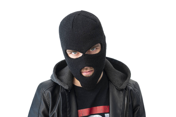 A thief in a black jacket. A man in a black balaclava with an evil expression on his face. An aggressive bandit isolated on a white background. The concept of crime or theft. - Photo, Image