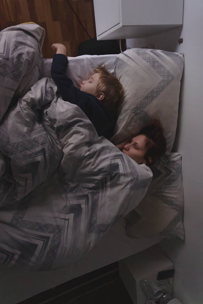 Een mama en een zoontje van drie slapen in het bed - bovenaanzicht - Foto, afbeelding