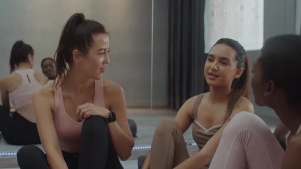 Handheld shot of three diverse female friends resting on floor after yoga class at studio - Footage, Video