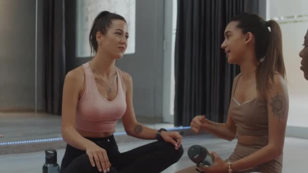 Media lunga possibilità di giovane donna che parla con le amiche mentre fa esercizio di stretching a lezione di yoga - Filmati, video