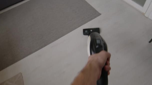POV-Aufnahme von unkenntlich gemachten Mann, der mit Handstaubsauger Fußboden im Wohnzimmer staubsaugt, während er am Wochenende Hausarbeit erledigt - Filmmaterial, Video
