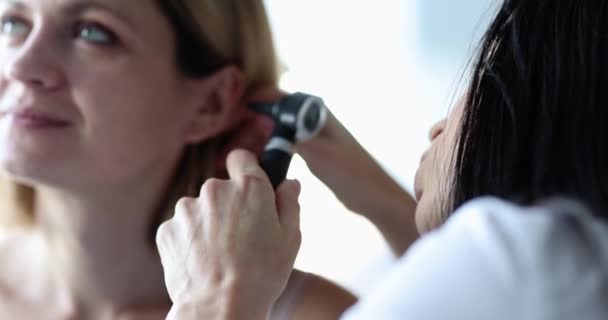 Um médico otorrinolaringologista olha para um close-up da orelha das mulheres. Ferramentas médicas para diagnosticar uma doença. Diagnóstico da perda auditiva - Filmagem, Vídeo