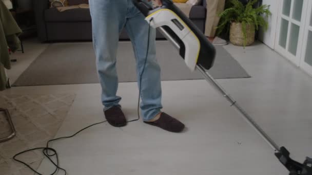 Joven hombre caucásico aspirando piso en la sala de estar mientras su esposa Biracial limpia superficies, haciendo tareas domésticas juntos el fin de semana - Metraje, vídeo