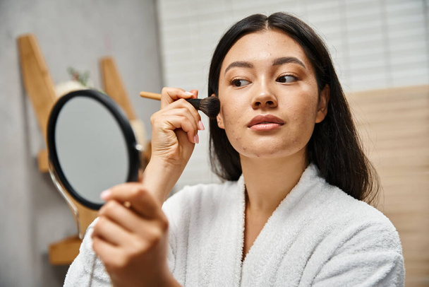 mujer asiática joven con cabello moreno y acné aplicando polvo con cepillo cosmético, problemas de piel - Foto, Imagen