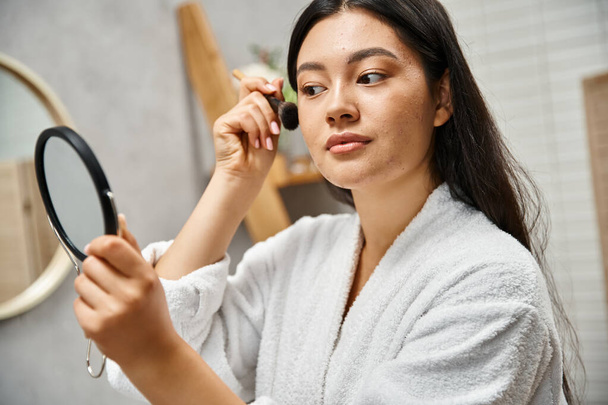 ziemlich asiatische Frau mit brünetten Haaren Make-up über Akne-anfällige Haut mit kosmetischen Pinsel - Foto, Bild